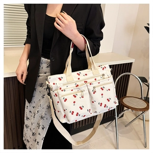 Detail view of large white canvas tote bag with red cherry prints and front zippers