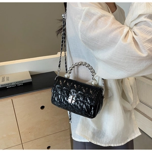 Detail of black quilted bag with silver bead handle and pearl accent worn by model