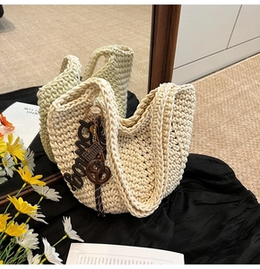 Détail du sac cabas au crochet blanc cassé avec breloques marron sur fond miroir