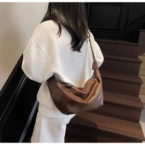 Detail of brown faux leather hobo bag showing arc seams and adjustable strap on stairs