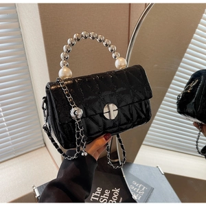 Detail of black quilted crossbody bag featuring a luxury pearl handle and chain strap