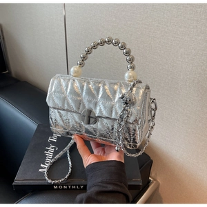 Detail view of silver quilted handbag with pearl beaded handle and metallic chain strap