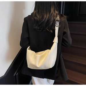 Detail of soft cream crescent tote bag featuring unique knot strap and stitching texture