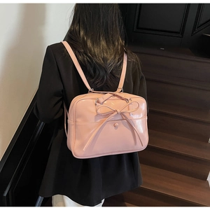 Pink patent leather tote with oversized bow detail worn as a stylish backpack