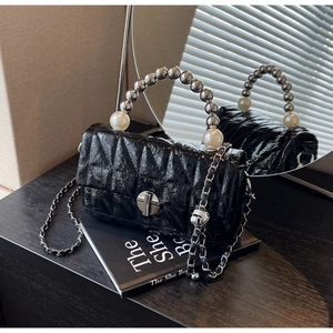 Detail of glossy black quilted handbag with pearl handle and metal twist lock