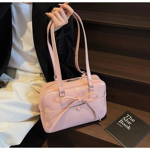 Close-up of a pink patent leather tote bag with a large bow detail on wooden stairs