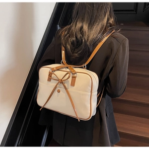 Detail of minimalist cream PU leather tote bag with brown bow on modern wooden stairs