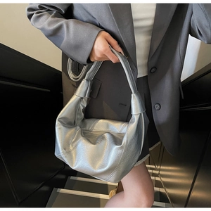 Close-up of metallic silver hobo bag with knotted handle detail on model in urban setting