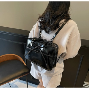 Close-up of a glossy black bow tote showing the backpack straps and sleek patent leather
