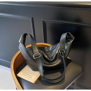 Detail of minimalist black leather hobo bag with silver buckle and knot design on strap