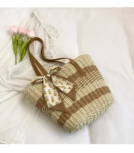 Detail of handwoven straw tote bag with color-block stripes and a floral scarf bow
