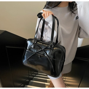 Detail of glossy black patent leather tote bag with a thin bow and long shoulder straps