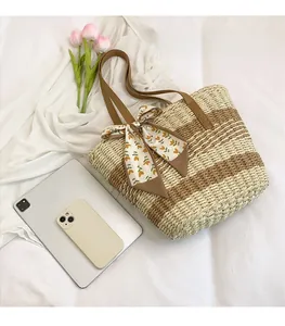 Flat lay of striped straw woven tote bag with floral ribbon and brown leather handles