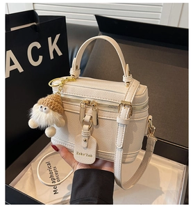 Close-up of a white lychee grain leather box bag with a gold zipper in a gift box