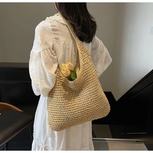 Detail of hand-woven straw tote bag with hollow knit pattern on a model shoulder