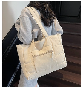 Détail d'un grand sac cabas matelassé beige avec poche zippée porté à l'épaule