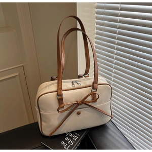 Detail of beige bow tote bag with brown handles and glossy finish on dark surface