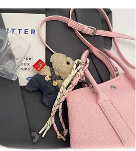 Détail du sac seau en cuir rose avec breloque d'ours en peluche sur un blazer gris