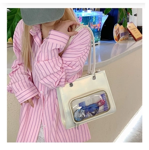 Detail of a cream faux leather Itabag with a clear window showing anime badges and cards