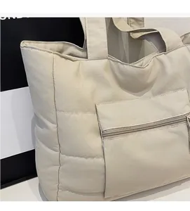 Gros plan d'un sac cabas matelassé beige montrant le tissu rembourré et la poche zippée