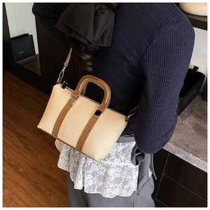 Detailed side view of beige straw handbag with brown leather straps worn on shoulder