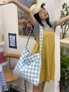 Detail of blue and white gingham canvas tote bag with wide shoulder strap and woven label