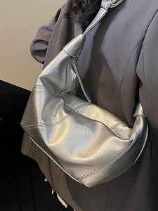Minimalist silver half-moon tote bag in metallic leather worn over a dark grey blazer