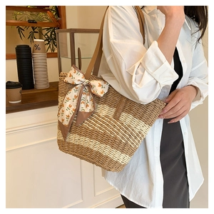 Detail of hand-woven straw tote with leather strap and orange floral bow decoration