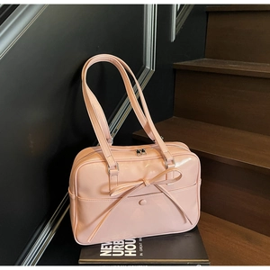 Detailed view of pink patent leather tote bag with bow accent on a wooden staircase