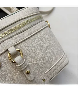 Detail shot of white pebble grain faux leather bag with gold-tone zipper and logo