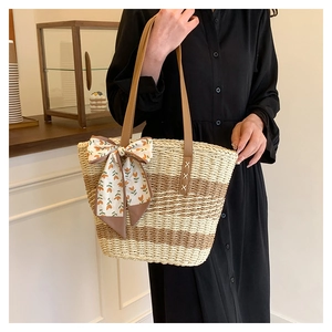 Macro shot of hand-woven straw tote with leather straps and floral silk scarf detail