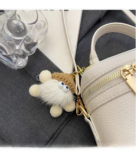 Detail of white plush monster bag charm with knit hat on a premium white leather handbag