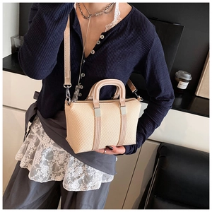 Detail of a beige woven crossbody bag featuring leather handles and silver hardware accents