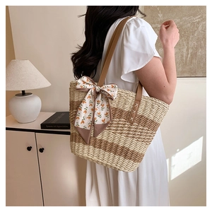 Detail of hand-woven straw bag with striped pattern and leather strap on model