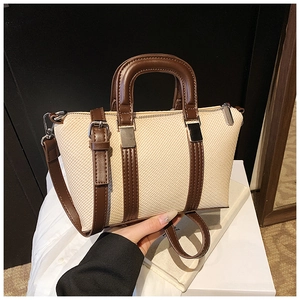 Detail view of woven cream fabric texture and brown leather straps on the handbag