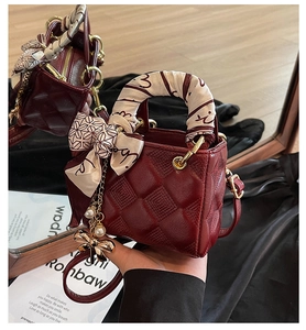 Close-up of wine red quilted handbag with scarf wrap handle and butterfly charm detail