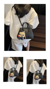 Détail du sac seau en cuir noir avec breloque ours porté sur un sweat à capuche blanc