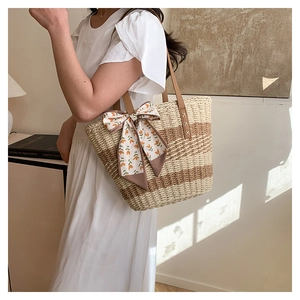 Detail of striped straw tote with leather handle and floral scarf on a white dress