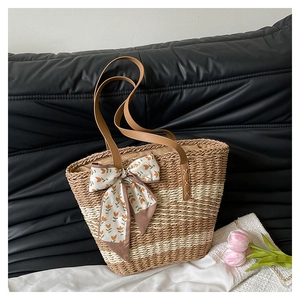 Detail of striped straw beach bag with floral ribbon bow and brown slim handles