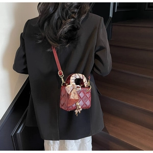 Detail of red quilted mini bag with decorative scarf handle and gold pearl charm pendant