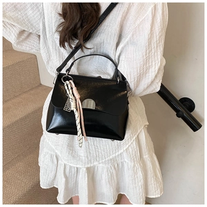 Detail of black glossy tote bag with silver lock and silk scarf on a white dress