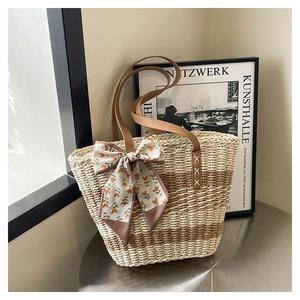 Close-up of woven straw tote bag featuring brown leather straps and floral silk scarf detail