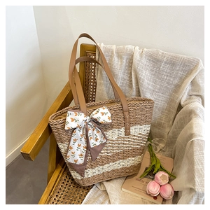 Detail of woven straw tote bag featuring contrast stripes and floral scarf ornament