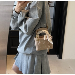 Detailed view of beige quilted mini handbag with decorative scarf and pearl charm on a model