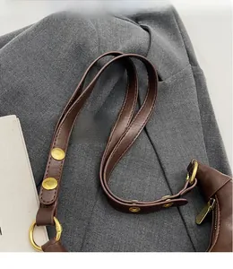 Detail of adjustable brown faux leather shoulder strap with polished gold metal buckles