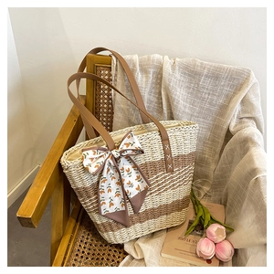 Detail of a striped woven straw tote bag with a brown leather strap and floral silk scarf