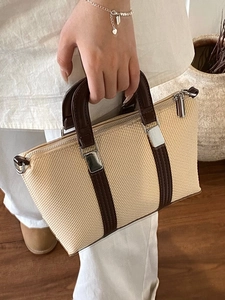 Chic beige woven handbag with dark brown leather straps held against a warm home backdrop