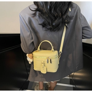Detail view of yellow box-shaped crossbody bag with plush bear charm on grey suit model