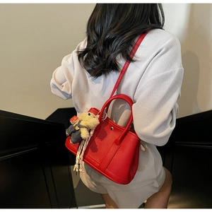 Sac seau en cuir rouge grainé porté en bandoulière par un mannequin avec un ours