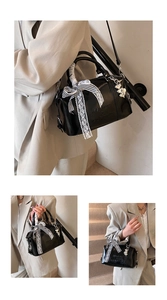 Detail of black Boston bag featuring ribbon bow, lace trim and silver heart charms